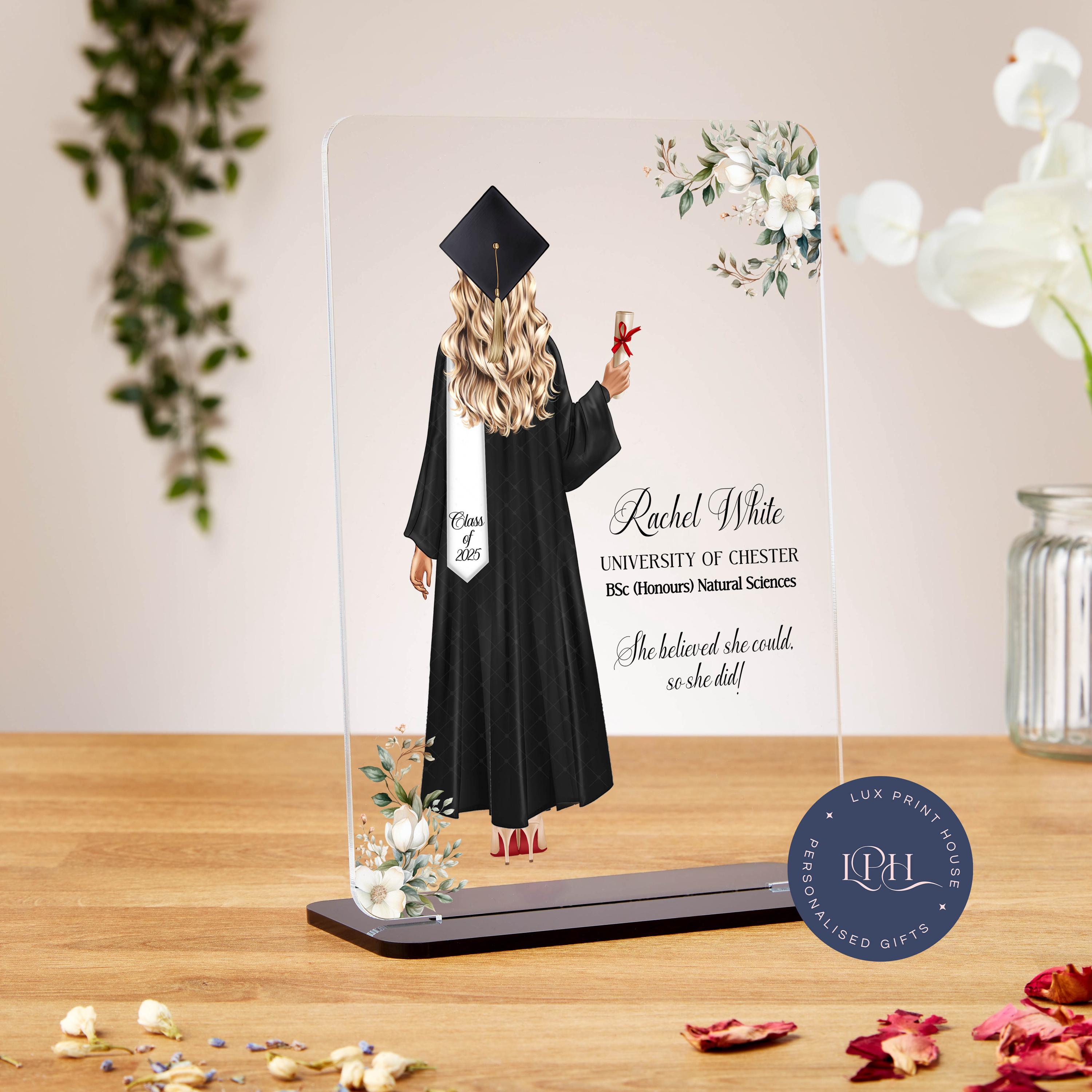 A graduation plaque featuring an illustration of a female graduate with long blonde hair wearing a black gown and graduation cap, holding a diploma tied with a red ribbon. Her white sash reads “Class of 2025.” The background includes soft floral accents in the corners. The text on the plaque reads: “Rachel White – UNIVERSITY OF CHESTER – BSc (Honours) Natural Sciences.” Below is the motivational quote: “She believed she could, so she did!” A circular logo at the bottom right corner says “Lux Print House – P