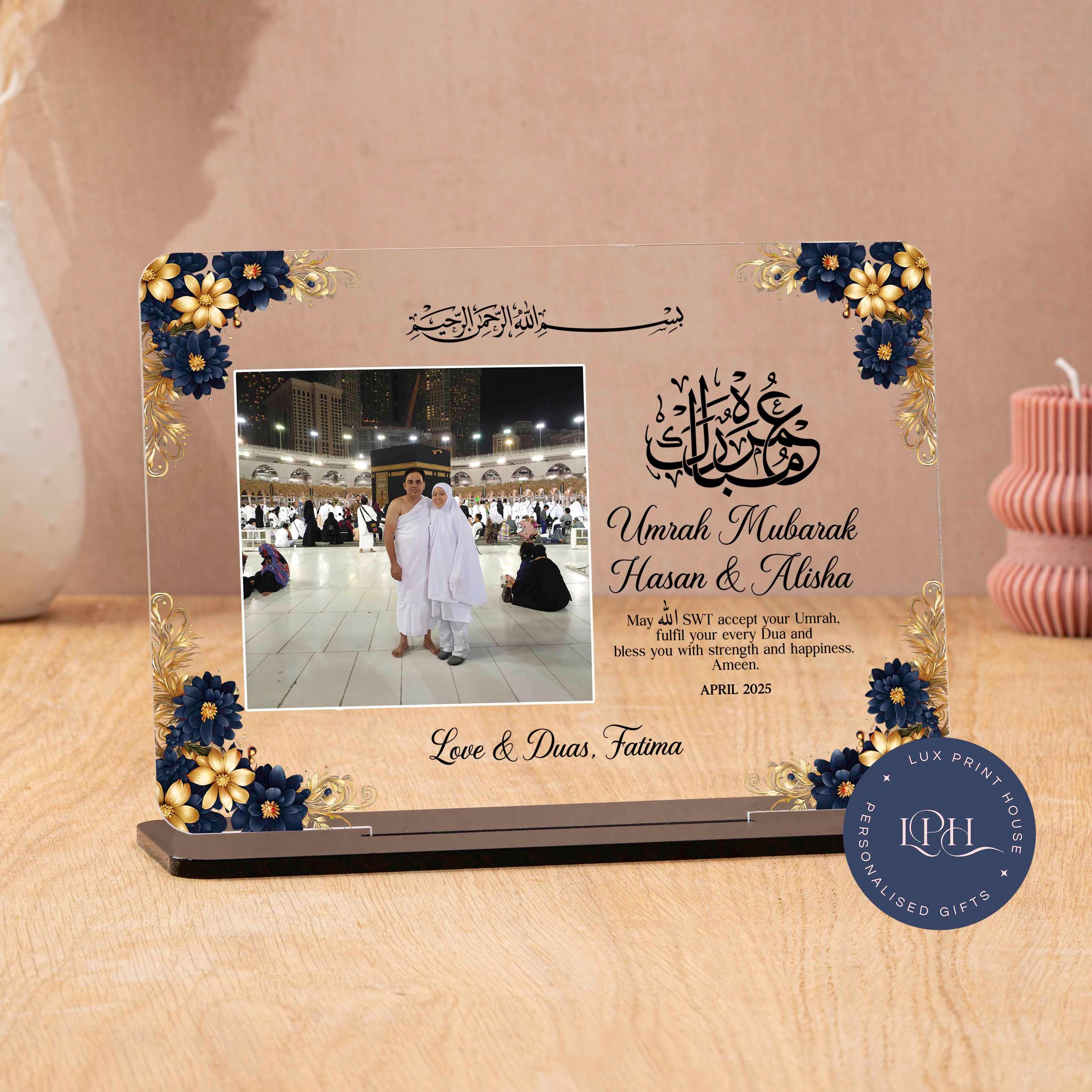 A personalised Umrah gift plaque featuring a real photo of a couple at the Kaaba, framed with ornate navy and gold floral accents. Arabic calligraphy at the top says “Umrah Mubarak,” accompanied by a heartfelt dua asking Allah to accept the Umrah and bless the recipients with strength and happiness. Includes space for custom names, a personal message, and a date. A meaningful Islamic keepsake to honour a sacred journey.