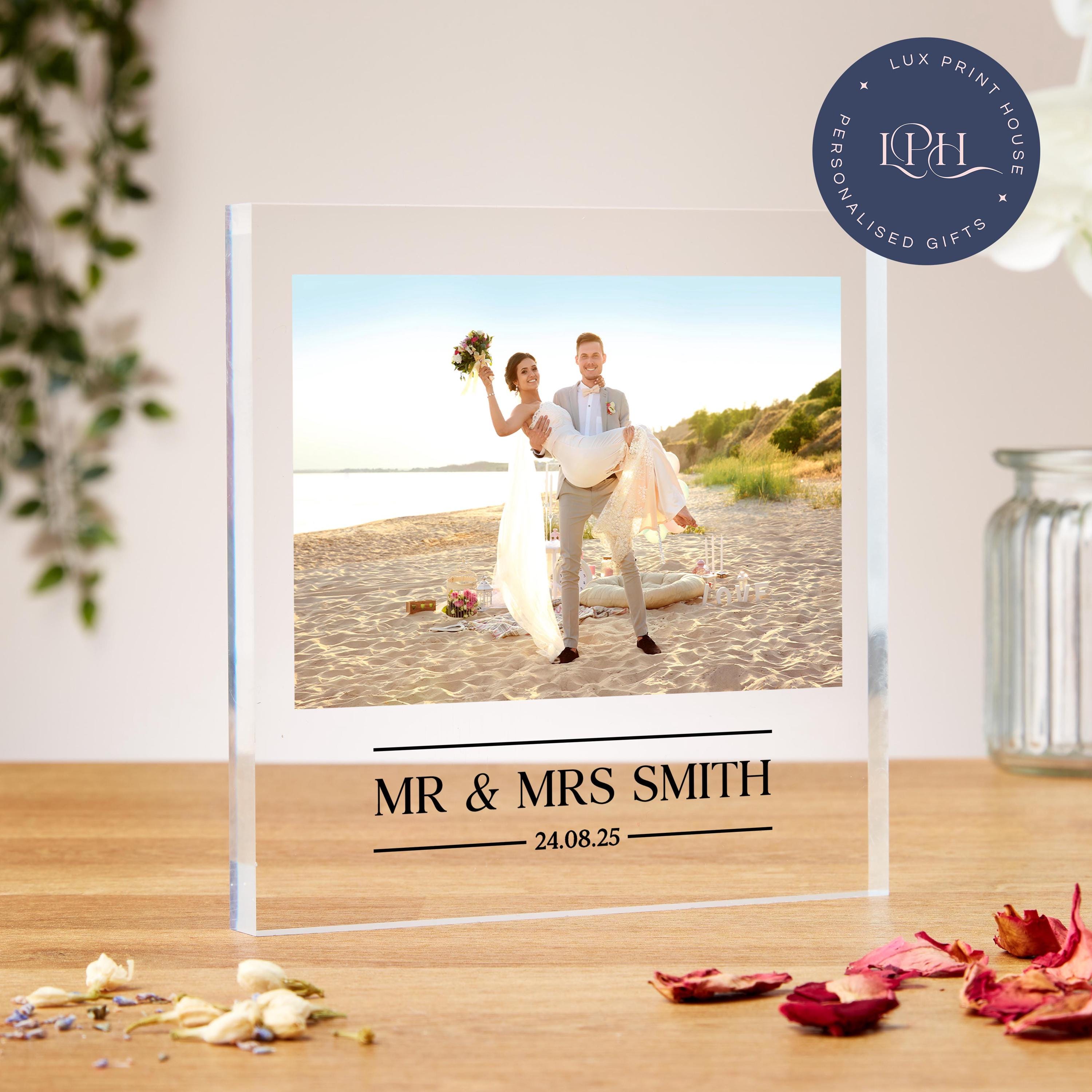 A personalised acrylic block featuring a romantic beach wedding photo with a groom playfully lifting his smiling bride, who holds a bouquet aloft. The sandy backdrop, picnic setup, and soft sunset lighting add charm. Below the photo, elegant custom text displays “Mr & Mrs” with the couple’s surname and wedding date. This custom keepsake makes a heartfelt gift for weddings, anniversaries, or newlyweds to treasure their special day.