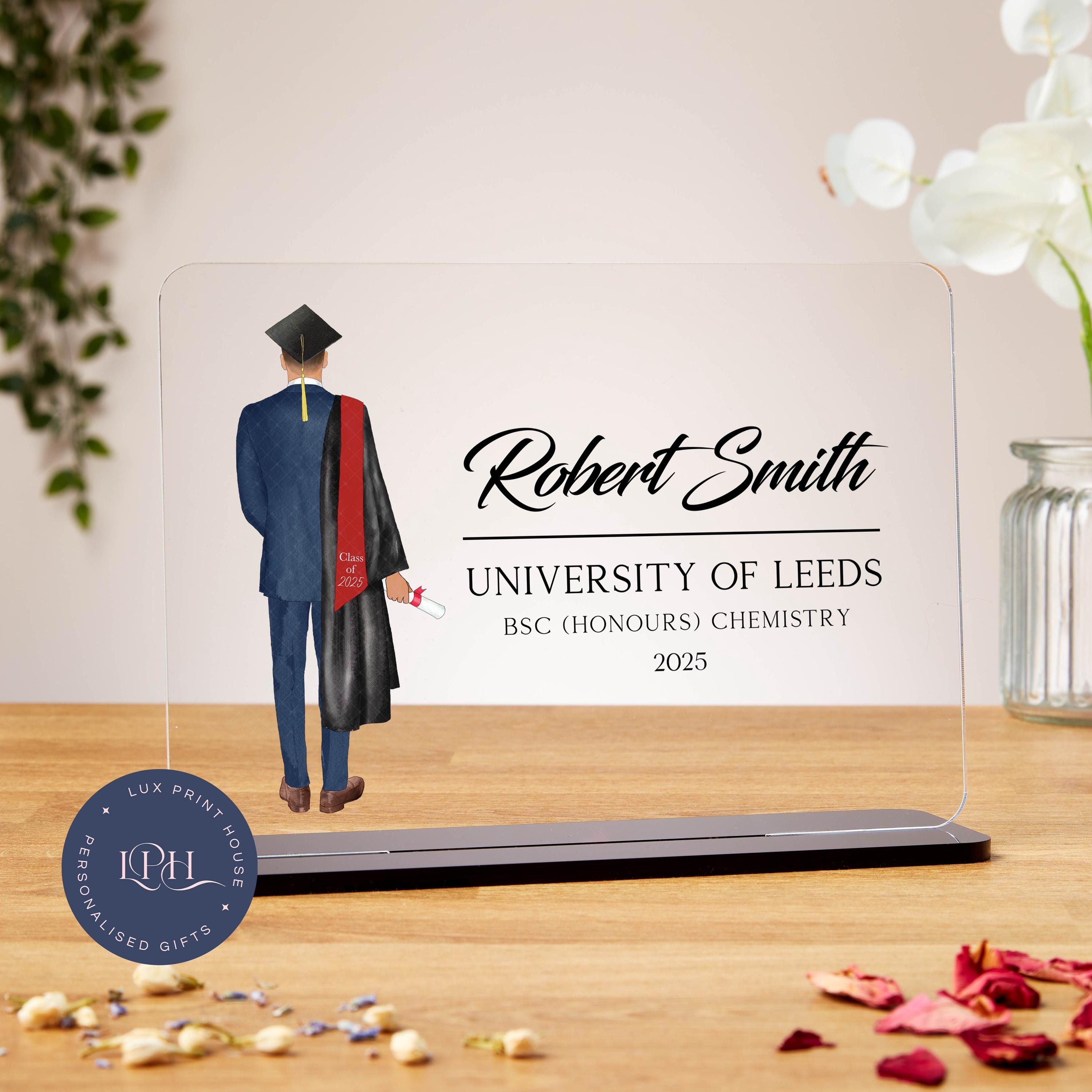 Graduation plaque featuring an illustration of a male graduate in a blue suit, black graduation gown, and cap with a gold tassel. He holds a diploma in one hand and has a red stole reading “Class of 2025.” The text beside him reads: “Robert Smith, University of Leeds, BSc (Honours) Chemistry, 2025.” The design is clean and modern, ideal for commemorating a graduation achievement.